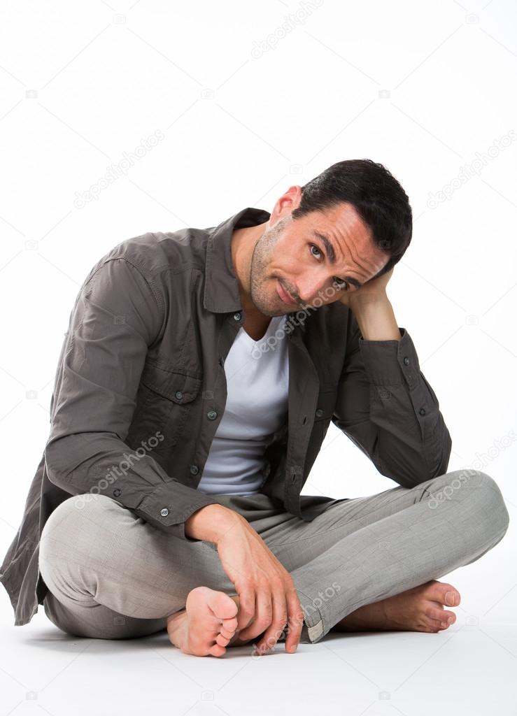 Thoughtful man sitted on the floor, looking at camera and holding his head with one hand