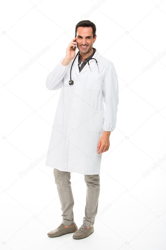 Full length portrait os a smiling male doctor with stethoscope while using a mobile phone