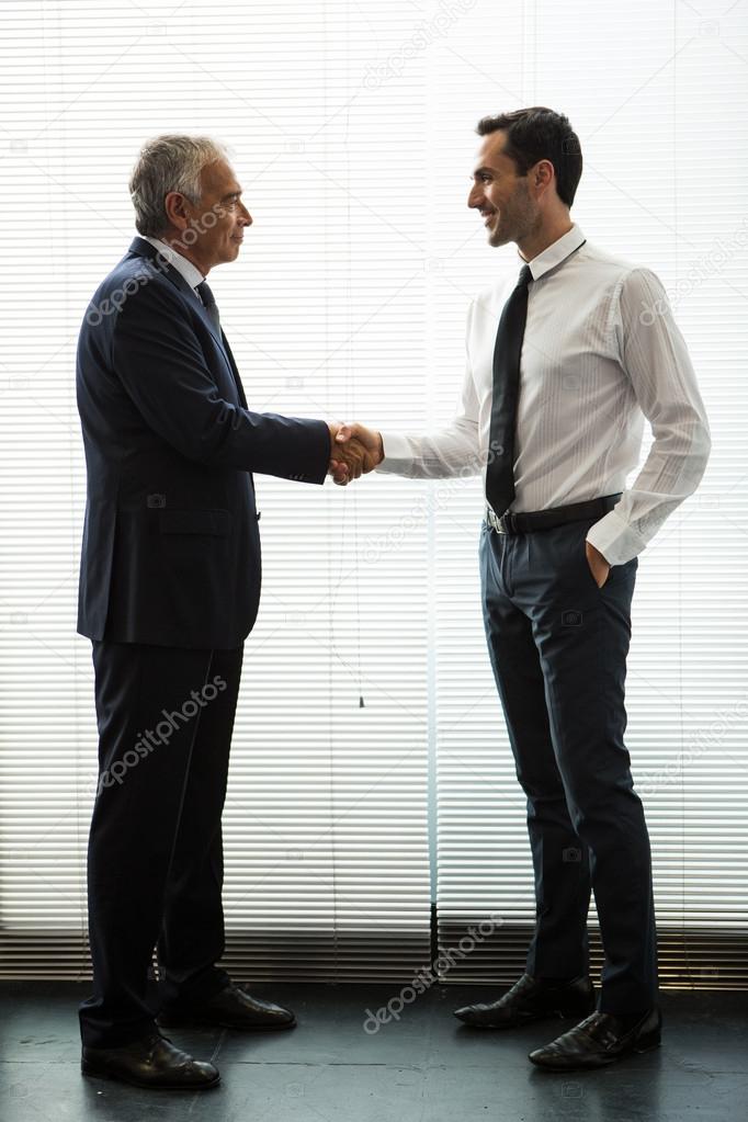 Full length portrait of two businessmen standing up, smiling and shaking hands