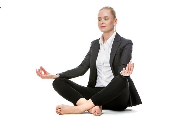 Mulher de negócios loira sentada no chão fazendo uma posição de ioga com os olhos fechados — Fotografia de Stock
