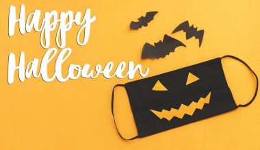 Kötü yüz maskesi üzerine Cadılar Bayramı mesajınız kutlu olsun. Turuncu arka planda Jack O Lantern gülüşü. 2020 Cadılar Bayramı, Coronavirus sırasında güvende olun. El yazısı, mevsimlik tebrik kartı.