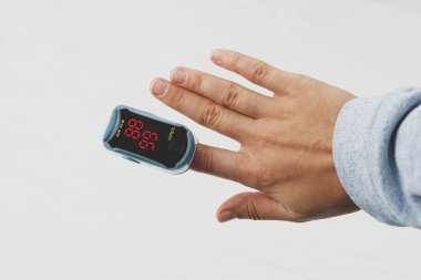 Nabız oksimetresi beyaz zemin üzerinde, kan oksijeni seviyesini ölçüyor. Taşınabilir Oksimetre Parmak ucu oksijen doygunluğunu test ediyor. Evde COVID-19 tespit edildi.