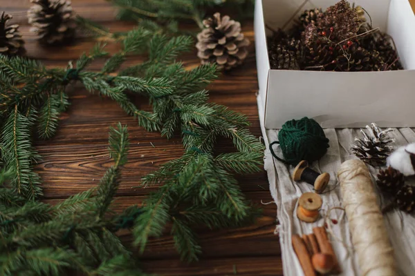 在木制桌子上做乡村圣诞花环 圣诞花环 带有浆果 松果和自然节庆装饰品 麻绳和乡村背景 — 图库照片