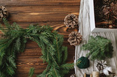 Ahşap masada rustik noel çelengi yapmak. Böğürtlenli Noel çelengi, yeşil köknar dalları, çam kozalakları ve kır arka planındaki doğal şenlik süslemeleri.