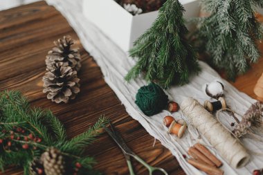 Ahşap masada rustik noel çelengi yapmak. Böğürtlenli Noel çelengi, yeşil dallar, kozalaklar ve doğal festival dekorasyonları, makas, sicim. Tatil atölyesi