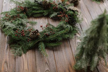 Kırmızı böğürtlenli modern Noel çelengi, yeşil dallar, çam kozalakları, kırsal arka planda doğal ağaç süslemeleri. Ahşap masada kırsal Noel çelengi. Mutlu Noeller.