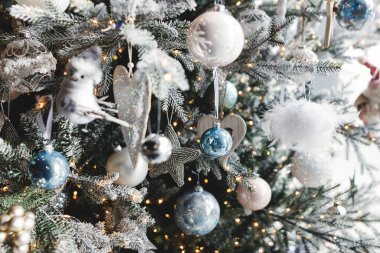 Şenlik odasında gümüş takılar ve ışıklar olan şık bir Noel ağacı. Beyaz topları, gümüş yıldızları ve oyuncakları olan modern Noel ağacı. Mutlu Noeller ve mutlu tatiller!