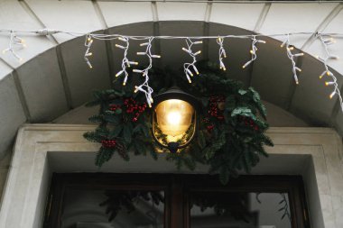 Kırmızı böğürtlen ve fenerle süslenmiş şık Noel dalları, mağaza önünde veya bina cephesinde modern süsler. Noel şenlikli sokak dekoru, tatil kış panayırı. Mutlu Noeller.