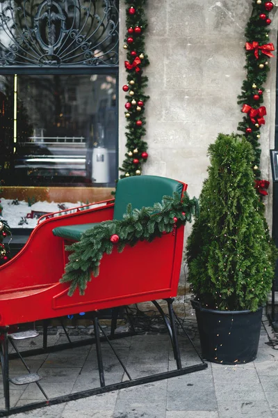 スタイリッシュなサンタ赤と緑のそりに乗るとクリスマスツリー 店頭や建物のファサードで現代的な装飾 クリスマスのお祝いの通りの装飾 休日の冬のフェア メリークリスマス — ストック写真