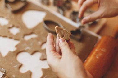 Noel tatili için elinde zencefilli kurabiye tutan kişi. Elleri zencefilli ekmek hamurunu noel ağacı metal kesicisiyle kır masasında baharatlar, şenlikli süslemeler, ışıklar...
