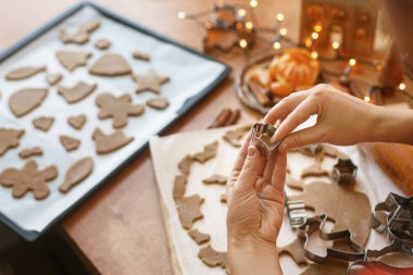 Kırsal masada zencefilli ekmek hamuru kesen elleri baharatlar, portakallar, şenlikli dekorasyonlar, ışıklar. Noel kurabiyesi yapan kişi, bayram gelişimi
