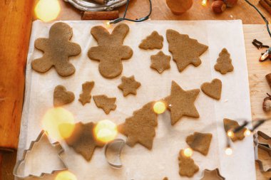 Şenlikli noel şekillerinde çiğ zencefilli kurabiyeler ve metal kesiciler, dekorasyonlar ve kırsal masada ışıklar. Zencefilli kurabiye pişirme, Noel tatili gelişimi.