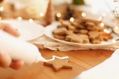 Kırsal masada kremalı zencefilli kurabiye süslemek. Noel tatili geleneği ve gelişimi. Elleri şekerli kurabiyelerle fırında pişmiş Noel kurabiyeleri süslüyordu. Aile zamanı.
