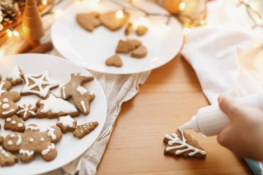 Zencefilli kurabiyeleri kırsal masada kremayla süslemek. Noel tatili geleneği ve gelişimi. Elleri şekerli kurabiyelerle fırında pişmiş Noel kurabiyeleri süslüyordu. Aile zamanı.