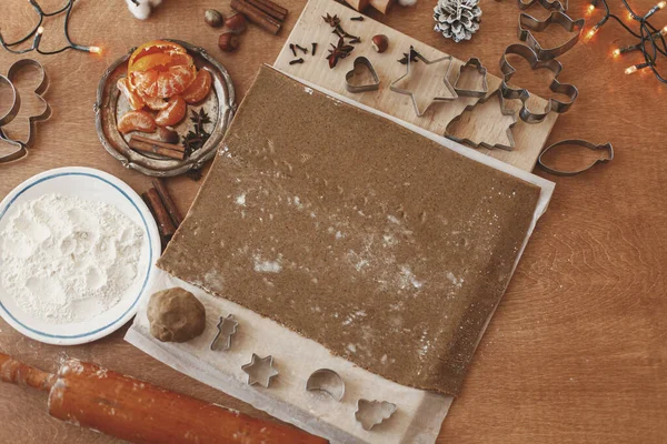Making gingerbread cookies flat lay, christmas advent. Raw gingerbread  dough, metal cutters ,flour, wooden rolling pin, spices, oranges, festive decorations on rustic table. Holiday tradition