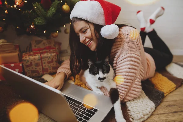Boldog Fiatal Télapó Kalapban Macskával Laptopot Néz Karácsonyfán Fényben Online — Stock Fotó