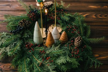 Mutlu Noeller! Modern el yapımı çelenk, küçük ağaçlar, mumlar ve çam kozalakları kırsal ahşap masa üzerinde, Noel sofrası. Evdeki tatil yemeği için şenlikli stil dekorasyonu..