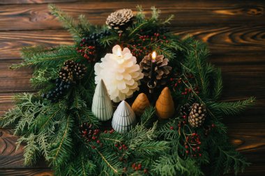 Mutlu Noeller! Modern el yapımı çelenk, küçük ağaçlar, mumlar ve çam kozalakları kırsal ahşap masa üzerinde, Noel sofrası. Evdeki tatil yemeği için şenlikli stil dekorasyonu..