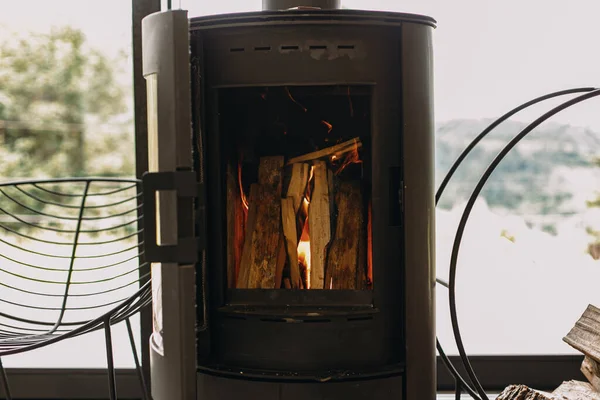 现代黑色壁炉与燃烧的火和木柴的金属站在大窗户的背景 寒冷季节里温暖祥和的时刻 舱房里加热器 — 图库照片