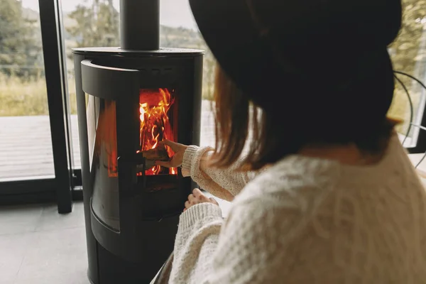 穿着针织毛衣的时髦女人用温暖的火把木柴放进现代的黑色壁炉 寒冷季节温暖舒适的时刻 河马女在山上舒适的小木屋里休息 — 图库照片