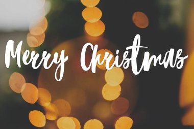 Bulanık noel ağacına ve altın ışıklara el yazısıyla mutlu noel mesajları, yeşil arka planda sarı ışıklandırma bokeh. Tebrik kartı, modern mevsimler selamları. İyi tatiller.