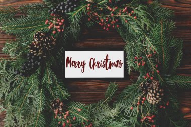 Mutlu Noeller mesajı telefon ekranında ahşap masa üzerindeki kırsal noel çelengiyle yazılmış, internette selamlar. Tebrik kartı, modern mevsimler selamları. İyi tatiller.