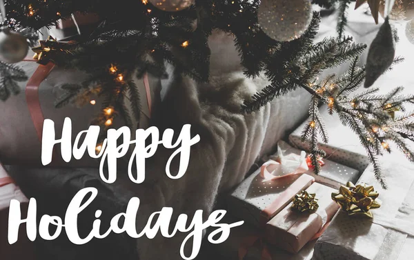 ハッピーホリデーグリーティングカード ゴールデンライトのクリスマスツリーの下にスタイリッシュなラップクリスマスギフトボックスに手書きの幸せな休日のテキスト 現代の季節の挨拶 — ストック写真