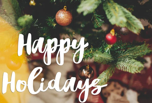 ラップされた贈り物やお祝いの光を背景に クリスマスツリー上の現代の金と赤の泡に手書きの幸せな休日のテキスト グリーティングカード現代の季節の挨拶 — ストック写真