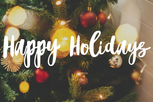 ハッピーホリデーグリーティングカード 赤と金の泡とお祝いの光と現代の装飾されたクリスマスツリーに手書きの幸せな休日のテキスト 現代の季節の挨拶 — ストック写真