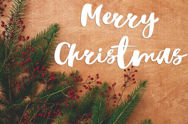 圣诞快乐 圣诞快乐的文字手写在枞树枝上 红色的浆果写在乡村的木头上 平铺在地板上 节日快乐 节日快乐 — 图库照片