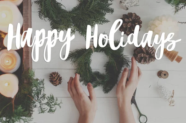 ハッピーホリデーグリーティングカード 手やろうそくの素朴なクリスマスの花輪に手書きの幸せな休日のテキスト 松のコーン 白い木のはさみ フラットレイアウト 現代の季節の挨拶 — ストック写真