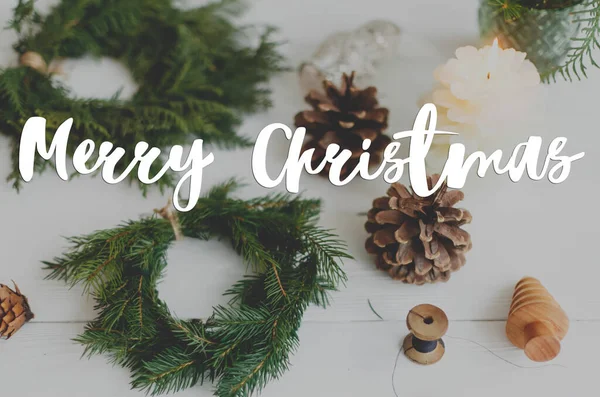 圣诞快乐文字手写在乡村圣诞花圈与蜡烛 松果和装饰的白色木材 现代佳节的问候 节日快乐 — 图库照片