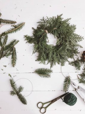 Kırsal çelenk, sedir ağacı ve köknar dallarını beyaz ahşap kırsal masa üzerinde makasla yapmak, üst manzara. Şenlikli el yapımı ev dekorasyonu. Mutlu Noeller ve mutlu Noeller.!