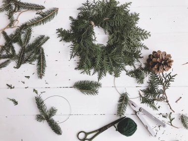 Kırsal çelenk, sedir ağacı ve köknar dallarını beyaz ahşap kırsal masa üzerinde makasla yapmak, üst manzara. Şenlikli el yapımı ev dekorasyonu. Mutlu Noeller ve mutlu Noeller.!