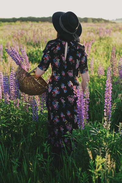 美丽时髦的女人在阳光灿烂的田野里 在柳条篮里采摘丁香 大气瞬息万变在乡村的夏季草地上 身着老式花衣头戴礼帽的年轻女性在休闲 — 图库照片