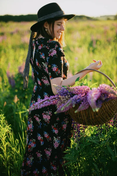 Güneşli Lup Tarlasında Hasır Sepet Çiçeklerle Yürüyen Şık Bir Kadın — Stok fotoğraf
