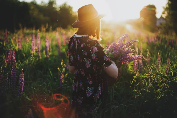 乡村田里 一个时髦的女人在夕阳西下的柳条筐里采摘丁香 大气瞬息万变在夏天的草地上采花的年轻女性 — 图库照片