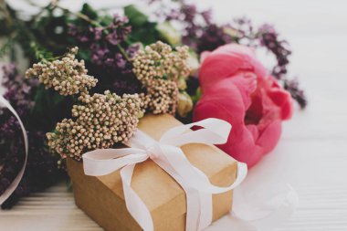 Anneler Günü ve Sevgililer Günü konsepti kutlu olsun. Beyaz ahşap arka planda şakayık, leylak ve gül desenli şık el sanatları hediye kutusu ve buket.