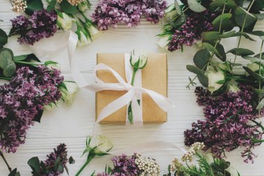 Leylak ve gül çiçekli şık bir hediye kutusu beyaz ahşap arka planda duruyordu. Anneler günün ve kadınlar günü konseptin kutlu olsun. Gül, kurdele ve çiçek kompozisyonu olan bir el işi.