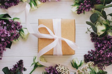 Leylak ve gül çiçekli şık bir hediye kutusu beyaz ahşap arka planda duruyordu. Anneler günün ve kadınlar günü konseptin kutlu olsun. Pembe kurdele ve çiçek kompozisyonu olan bir el işi.