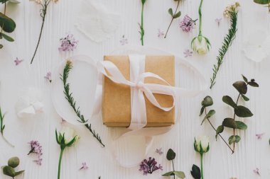 Leylak, gül, çiçek ve okaliptüs yapraklı şık bir hediye kutusu beyaz ahşap arka planda yatıyordu. Anneler günün ve kadınlar günü konseptin kutlu olsun. Kurdele ve çiçek kompozisyonu olan bir el işi.