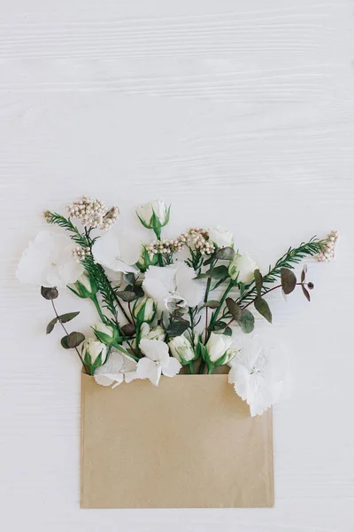 白い木にクラフトエンベロープから成長したスタイリッシュなバラ アジサイ ユーカリの枝 コピースペースのフラットレイアウト 花グリーティングカードと花配達 幸せな女性の日 — ストック写真