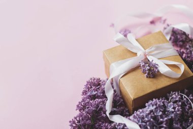 Leylak çiçekleri ve hediye paketi üzerinde fotokopi alanı olan pembe bir kağıt. Anneler günün ve kadınlar günü konseptin kutlu olsun. Bahar çiçekli tebrik kartı. Mor leylak buketi, şık bir zanaat ve kurdele mevcut.