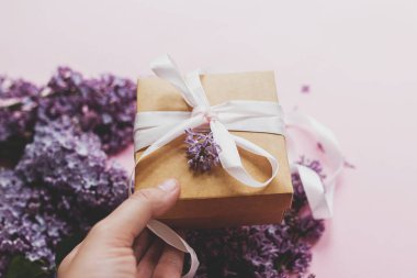 Hediye vermek, hediye paketi, kurdele ve pembe kağıt üzerinde leylak çiçekleri. Anneler günün ve sevgililer günü konseptin kutlu olsun. Mor leylak çiçeği buketi ve el işi hediye kutusu..