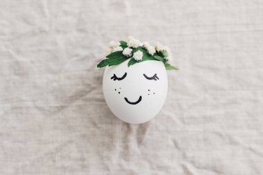 Mutlu Paskalyalar! Doğal yumurta, uyuyan yüzü çizilmiş ve keten kumaşında çiçekli bir taç takıyor. Çevre dostu sıfır atık tatil konsepti. Metin için boşluk olan üst görünüm