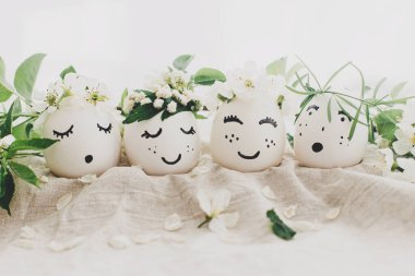 Mutlu Paskalyalar! Çiçek desenli keten kumaşlı, çiçekli çelenklerle süslü doğal yumurtalar, yumuşak ışıkta çiçek yaprakları ve yeşil yapraklar. Çevre dostu sıfır atık tatil kavramı