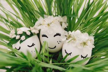 Çevre dostu sıfır ziyan tatili. Çiçekli çelenklerde uyuyan yüzler çizilmiş paskalya yumurtaları yumuşak ışıkta yeşil çimlerde. Mutlu Paskalyalar ve Paskalya Avları konsepti! Metin için boşluk