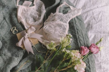 Şık bir hediye kutusu, modern mücevherler ve yatağında iç çamaşırı olan yeşil süveter üzerindeki bahar çiçekleri. Yumuşak kadınsı imaj, ev kavramında şehvetli ruh hali. Mutlu Kadınlar Günü, kadın zorunlulukları