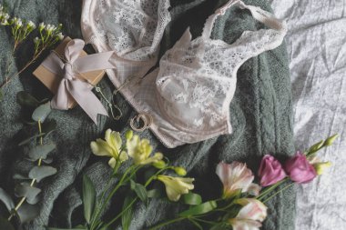 Şık bir hediye kutusu, modern mücevherler ve yatağında iç çamaşırı olan yeşil süveter üzerindeki bahar çiçekleri. Yumuşak kadınsı imaj, ev kavramında şehvetli ruh hali. Mutlu Kadınlar Günü, kadın zorunlulukları