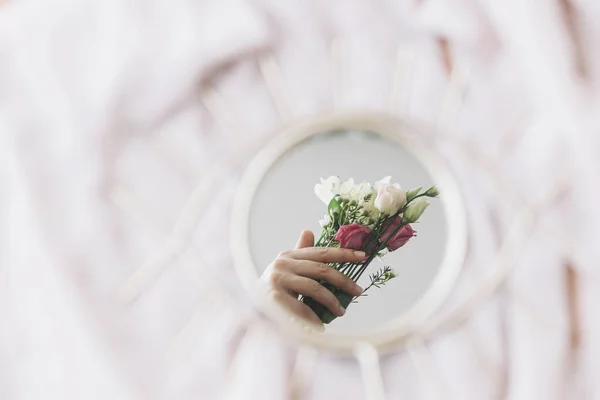 Hand holding flowers reflected in mirror on background of soft fabric. Hello spring and floral scent. Happy Women's and Mothers day. Mental Health concept. Gentle image